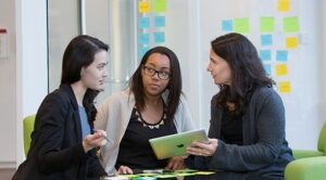 Three women in a discussion over an electronic tablet.