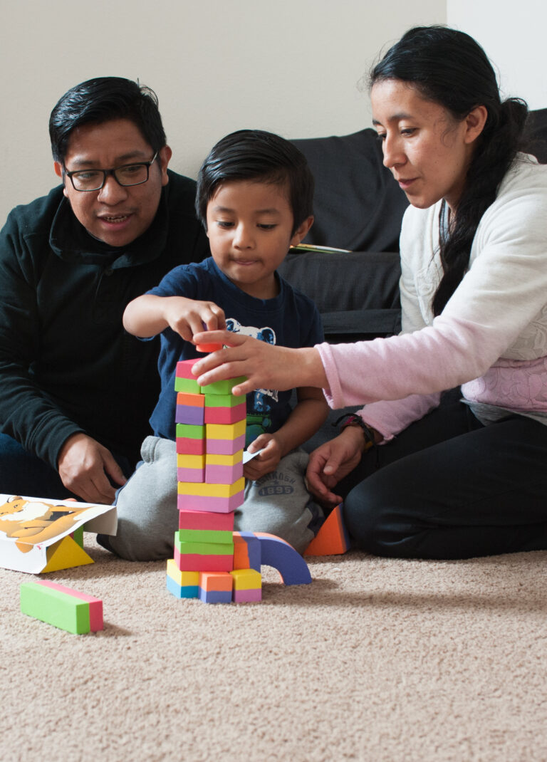 A child and two adults build a tower of blocks together.